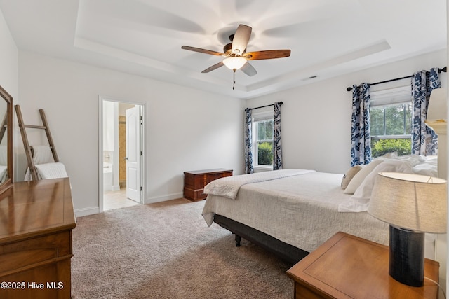 6005 Otter Tail Trl, Wilmington, NC 28412 - bedroom featuring a tray ceiling, multiple windows, light colored carpet, and ensuite bath