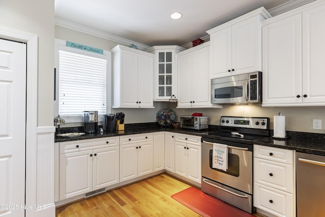 209 Georgia Ave, Carolina Beach, NC 28428 - kitchen featuring appliances with stainless steel finishes, white cabinetry, glass insert cabinets, light wood-style floors, and crown molding