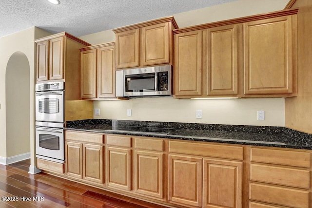 205 S Grist Mill Rd, Hampstead, NC 28443 - kitchen with appliances with stainless steel finishes, dark wood-type flooring, arched walkways, dark stone countertops, and a textured ceiling
