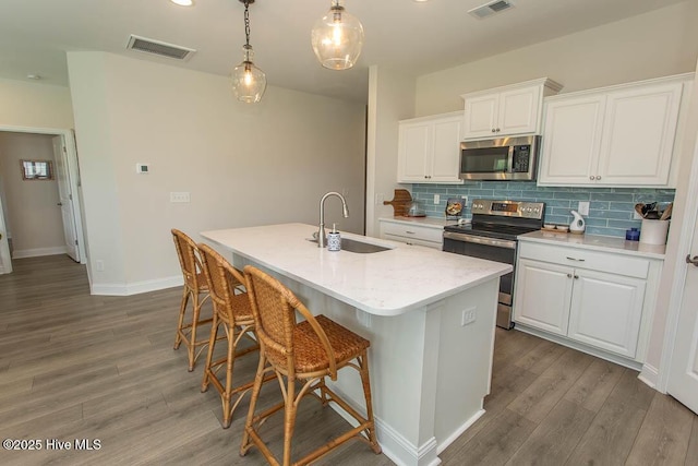 873 Bourne Dr SW, Ocean Isle Beach, NC 28469 - kitchen with stainless steel appliances, a sink, wood finished floors, a kitchen island with sink, and white cabinets