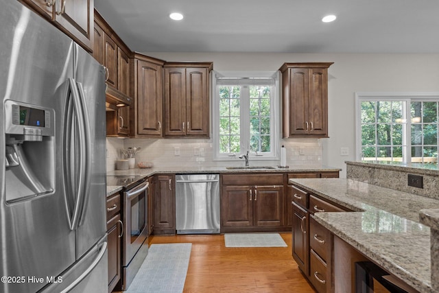 103 Sandspur Ln, West End, NC 27376 - kitchen featuring stainless steel appliances, a sink, light stone counters, light wood-type flooring, and backsplash