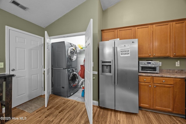 3106 John Willis Rd, New Bern, NC 28562 - kitchen featuring stainless steel refrigerator with ice dispenser, estacked washer and dryer, vaulted ceiling, brown cabinetry, and a textured ceiling
