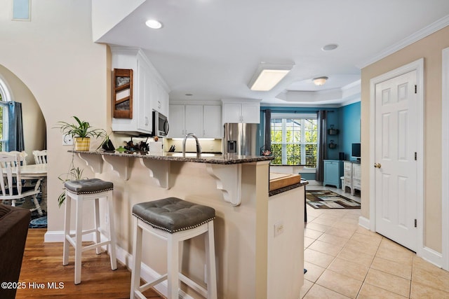 3052 Woods Walk Way, Rocky Mount, NC 27804 - kitchen with stainless steel appliances, a peninsula, white cabinetry, a breakfast bar area, and dark stone counters