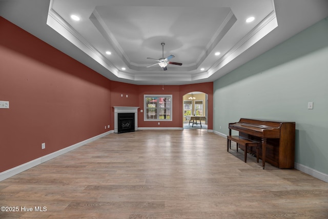 1006 Kingfish Way, New Bern, NC 28562 - unfurnished living room with arched walkways, a tray ceiling, baseboards, ceiling fan, and light wood-style flooring