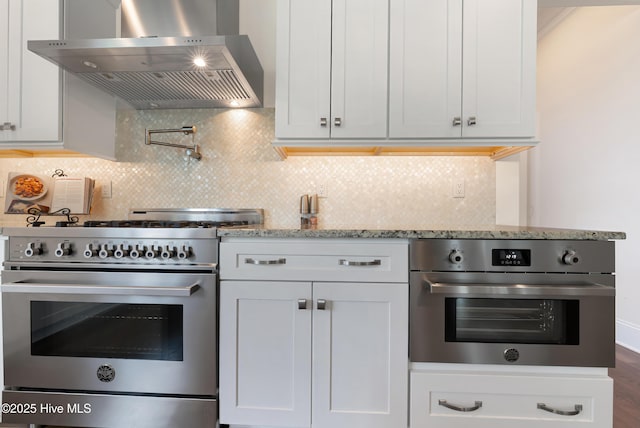 2570 Sugar Maple Ct, Southport, NC 28461 - kitchen featuring wall chimney range hood, stainless steel appliances, light stone countertops, tasteful backsplash, and white cabinets