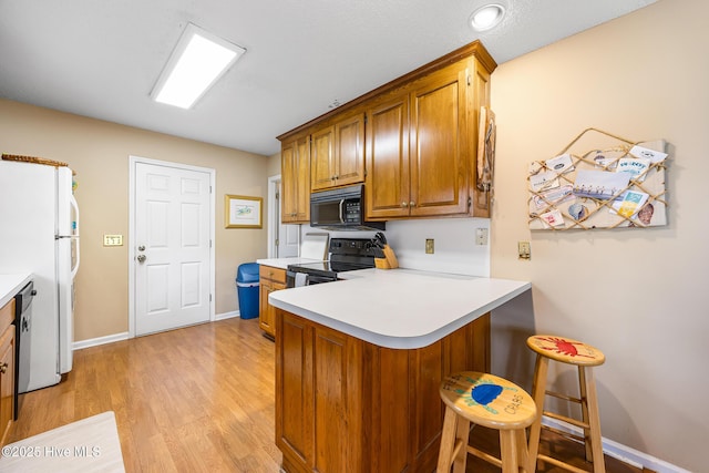 1137 Indigo Cir, Sunset Beach, NC 28468 - kitchen featuring black appliances, brown cabinets, a peninsula, a kitchen bar, and light countertops