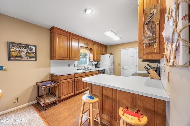 1137 Indigo Cir, Sunset Beach, NC 28468 - kitchen featuring freestanding refrigerator, a sink, brown cabinetry, a peninsula, and light countertops