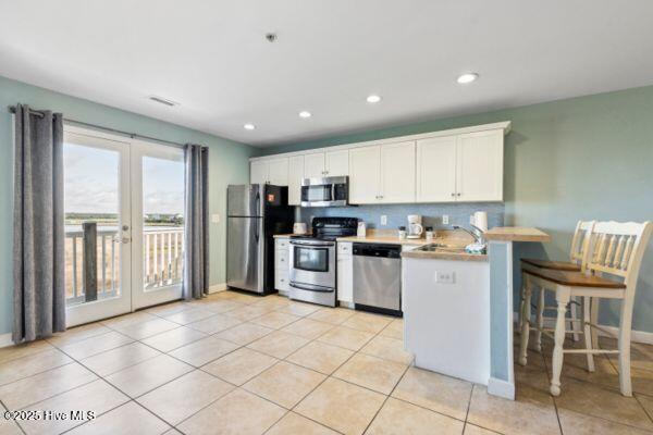 1505 N New River Dr Unit 210, Surf City, NC 28445 - kitchen featuring appliances with stainless steel finishes, french doors, a sink, a peninsula, and white cabinetry