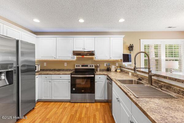 1135 Sunburst Way, Leland, NC 28451 - kitchen with stainless steel appliances, under cabinet range hood, a sink, a textured ceiling, and white cabinetry