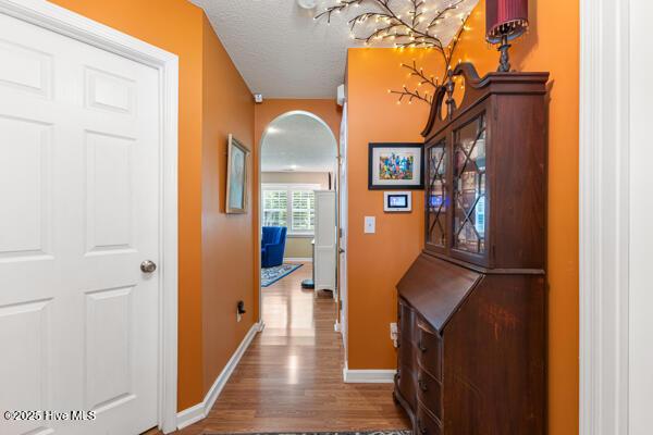 1135 Sunburst Way, Leland, NC 28451 - hallway featuring arched walkways, baseboards, wood finished floors, a textured ceiling, and a chandelier