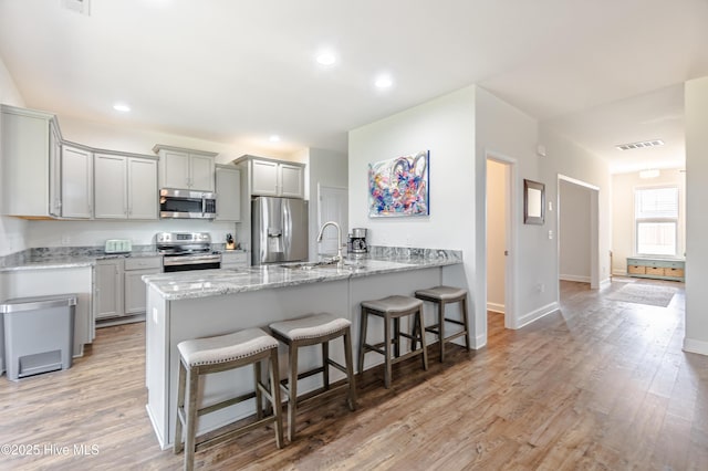 522 Heartwood Dr, Leland, NC 28479 - kitchen featuring stainless steel appliances, a peninsula, a breakfast bar area, gray cabinets, and light stone countertops