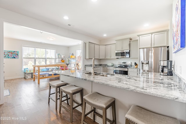 522 Heartwood Dr, Leland, NC 28479 - kitchen featuring appliances with stainless steel finishes, a sink, a peninsula, gray cabinetry, and a kitchen bar
