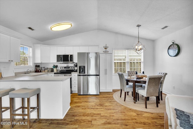 222 Bridgeton Ct, Wilmington, NC 28411 - kitchen featuring stainless steel appliances, vaulted ceiling, light wood finished floors, a chandelier, and white cabinets
