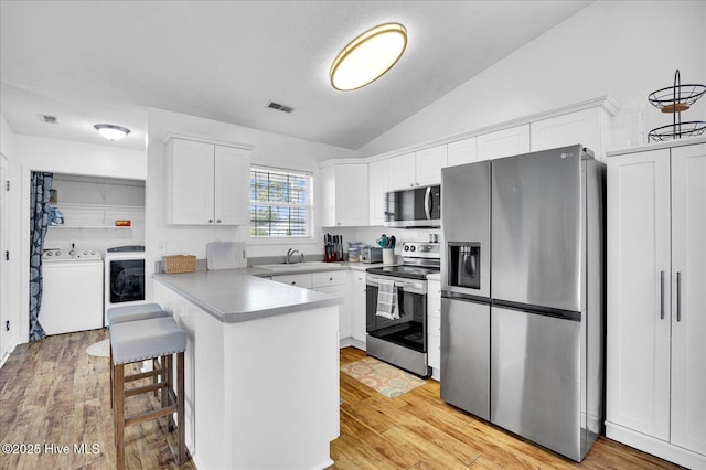222 Bridgeton Ct, Wilmington, NC 28411 - kitchen featuring stainless steel appliances, washer / dryer, a peninsula, white cabinetry, and lofted ceiling