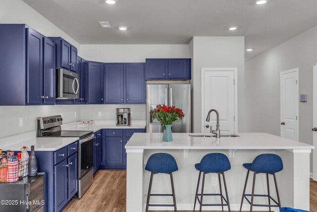 6751 Blacktip Ln, Wilmington, NC 28412 - kitchen featuring appliances with stainless steel finishes, blue cabinetry, a breakfast bar, light wood-style flooring, and recessed lighting