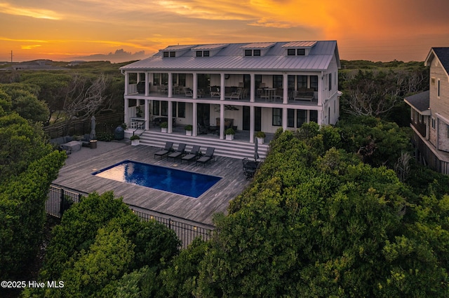585 Forest Dunes Dr, Pine Knoll Shores, NC 28512 - back of house at dusk with a balcony, a standing seam roof, an outdoor pool, a metal roof, and a patio