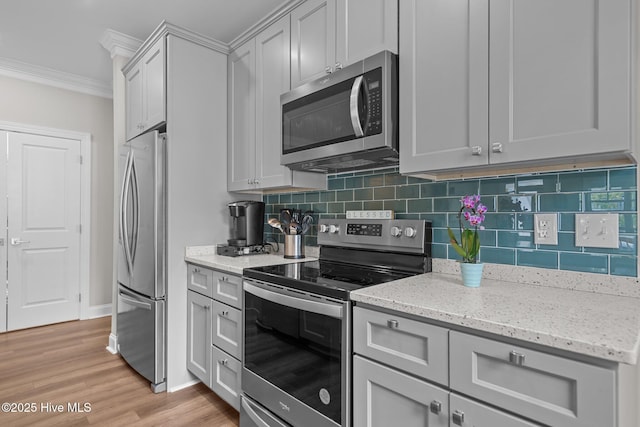 163 NE 31st St, Oak Island, NC 28465 - kitchen featuring appliances with stainless steel finishes, ornamental molding, tasteful backsplash, light stone counters, and light wood-style flooring