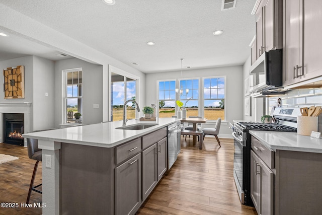 101 Claire Ct, Moyock, NC 27958 - kitchen featuring appliances with stainless steel finishes, a sink, a kitchen island with sink, dark wood-style flooring, and a glass covered fireplace