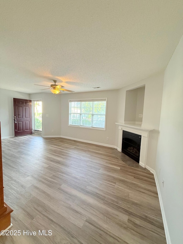 2104 Flagstone Ct Unit A-4, Greenville, NC 27834 - unfurnished living room featuring a textured ceiling, a fireplace, a ceiling fan, light wood-type flooring, and baseboards