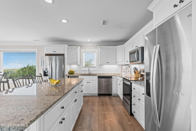 1239 Ocean Blvd W, Holden Beach, NC 28462 - kitchen featuring stainless steel appliances, white cabinetry, ornamental molding, dark wood finished floors, and light stone counters