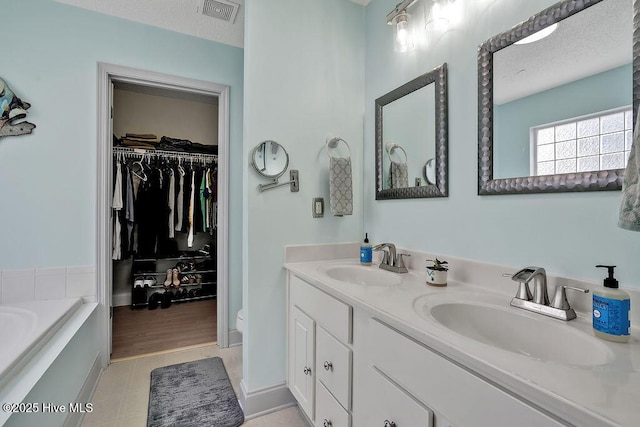 648 Pine Branches Cir SE, Leland, NC 28451 - bathroom featuring double vanity, a garden tub, a spacious closet, and a textured ceiling
