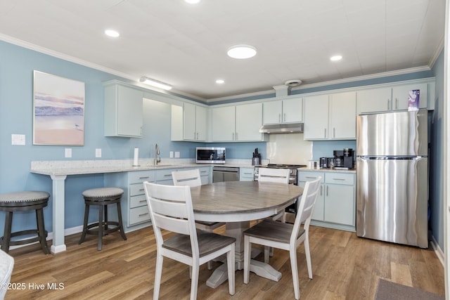 901 Ocean Dr, Emerald Isle, NC 28594 - kitchen featuring stainless steel appliances, under cabinet range hood, ornamental molding, a sink, and light wood-style flooring