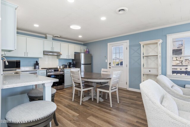 901 Ocean Dr, Emerald Isle, NC 28594 - kitchen with appliances with stainless steel finishes, under cabinet range hood, crown molding, healthy amount of natural light, and dark wood-style floors