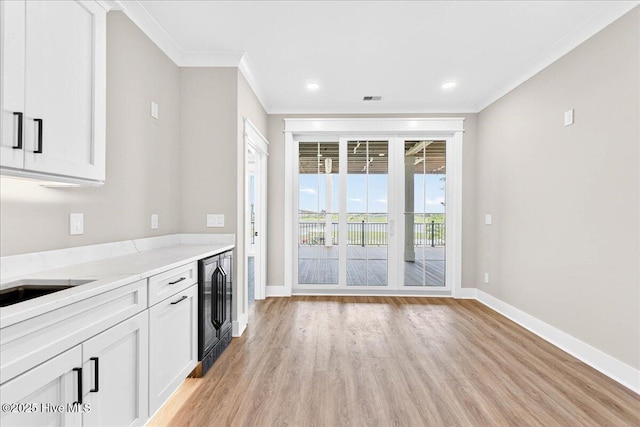 1711 Hemingway Dr SW, Ocean Isle Beach, NC 28469 - kitchen featuring light wood finished floors, ornamental molding, beverage cooler, baseboards, and white cabinetry