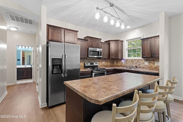 5709 Burgaw Hwy, Maple Hill, NC 28454 - kitchen featuring appliances with stainless steel finishes, dark brown cabinets, a center island, light wood-style flooring, and decorative backsplash