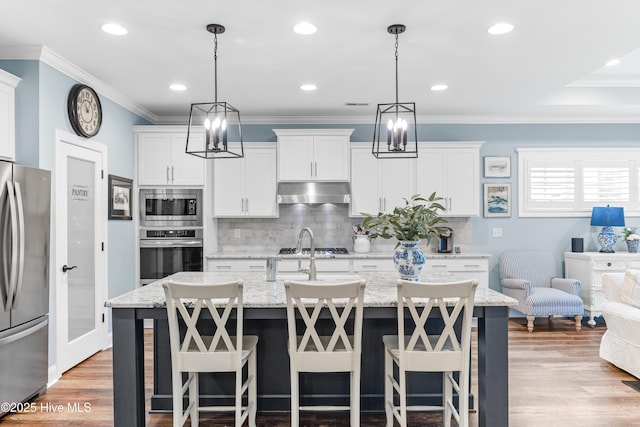 8116 Barstow Ln, Wilmington, NC 28411 - kitchen with stainless steel appliances, under cabinet range hood, an island with sink, backsplash, and white cabinets