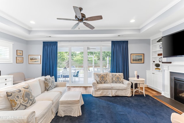 8116 Barstow Ln, Wilmington, NC 28411 - living room featuring a tray ceiling, crown molding, ceiling fan, a glass covered fireplace, and dark wood-style flooring