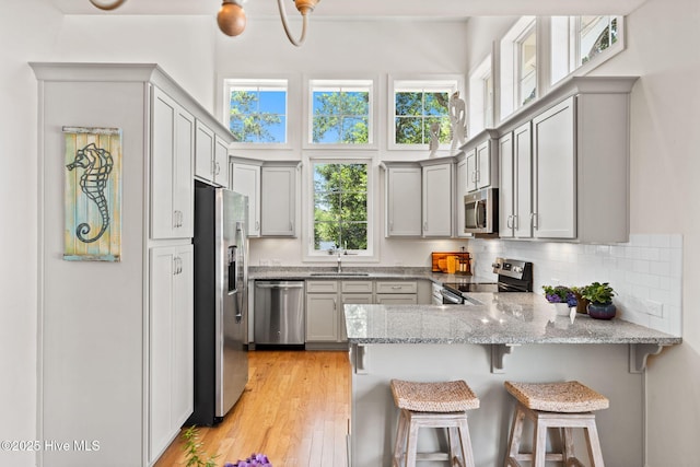 322 NE 42nd St, Oak Island, NC 28465 - kitchen featuring appliances with stainless steel finishes, a peninsula, gray cabinetry, light stone countertops, and a kitchen bar