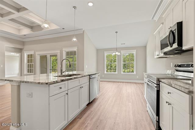 414 Laurel Ct NW, Calabash, NC 28467 - kitchen featuring appliances with stainless steel finishes, white cabinetry, light wood-style floors, an island with sink, and beamed ceiling