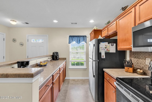 2129 Cass Lake Dr, Calabash, NC 28467 - kitchen with appliances with stainless steel finishes, decorative backsplash, brown cabinets, a peninsula, and recessed lighting