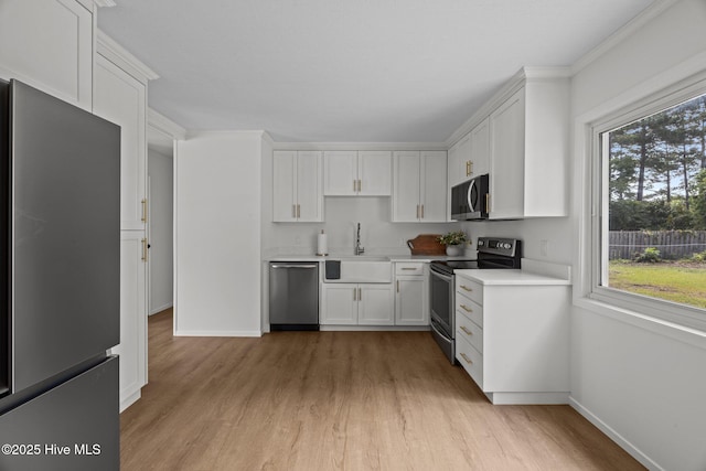 2402 S Lakeview Dr, Newport, NC 28570 - kitchen featuring stainless steel appliances, light wood-style floors, healthy amount of natural light, white cabinets, and ornamental molding