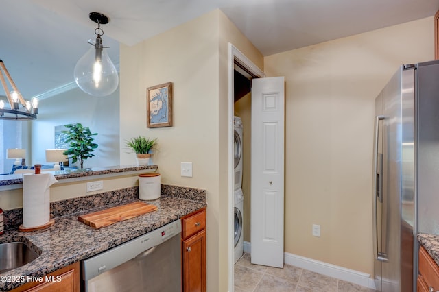 203 Sky Sail Blvd, New Bern, NC 28560 - kitchen featuring appliances with stainless steel finishes, stacked washer and clothes dryer, brown cabinetry, dark stone counters, and pendant lighting