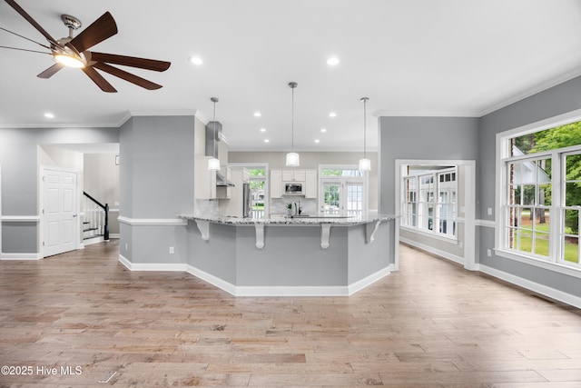 376 Red Fox Run Dr, Wallace, NC 28466 - kitchen featuring stainless steel microwave, white cabinets, a kitchen breakfast bar, crown molding, and light wood-style floors