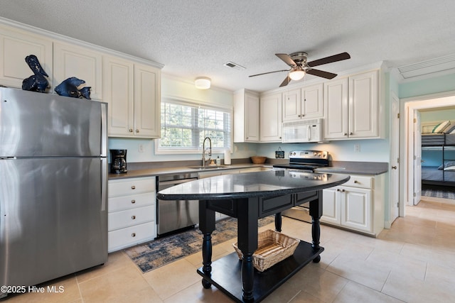 316 E Dolphin Dr, Oak Island, NC 28465 - kitchen with appliances with stainless steel finishes, a ceiling fan, white cabinetry, light tile patterned flooring, and a textured ceiling