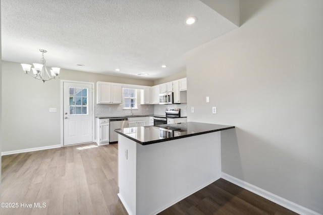 802 Mayfield Ct, Wilmington, NC 28411 - kitchen featuring appliances with stainless steel finishes, a peninsula, white cabinets, tasteful backsplash, and wood finished floors