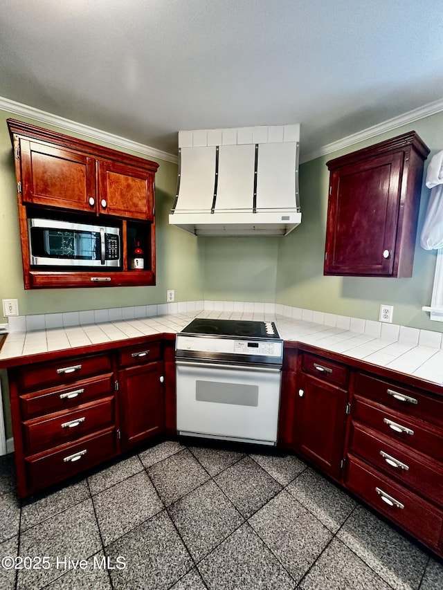 9550 NC-171, Williamston, NC 27892 - kitchen featuring white electric range oven, stainless steel microwave, ventilation hood, crown molding, and reddish brown cabinets