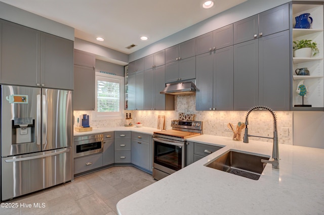 8508 Hammock Dunes Dr, Wilmington, NC 28411 - kitchen with appliances with stainless steel finishes, under cabinet range hood, gray cabinets, tasteful backsplash, and light stone counters
