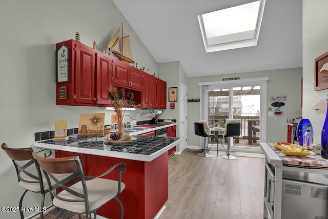 1785 New River Inlet Rd Unit 2, North Topsail Beach, NC 28460 - kitchen with light wood-style flooring, a peninsula, vaulted ceiling, dark brown cabinets, and a skylight