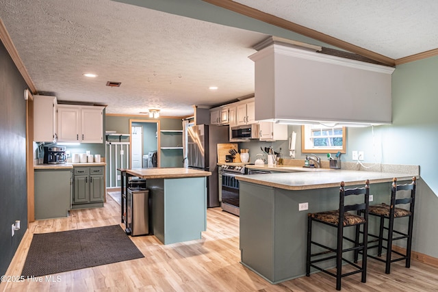 1360 Rays Bridge Rd, Whispering Pines, NC 28327 - kitchen featuring a textured ceiling, appliances with stainless steel finishes, crown molding, light wood-style floors, and a peninsula