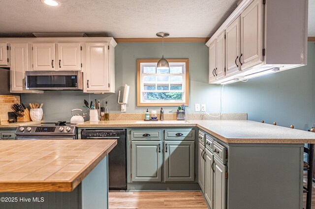 1360 Rays Bridge Rd, Whispering Pines, NC 28327 - kitchen featuring stainless steel appliances, a textured ceiling, light wood finished floors, white cabinetry, and hanging light fixtures