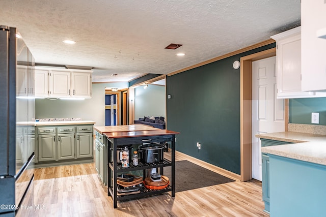 1360 Rays Bridge Rd, Whispering Pines, NC 28327 - kitchen featuring white cabinets, light countertops, ornamental molding, a textured ceiling, and light wood finished floors