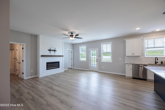 6001 Farmwood Loop, Wilson, NC 27896 - kitchen with stainless steel dishwasher, white cabinetry, a large fireplace, light stone counters, and light wood-style flooring