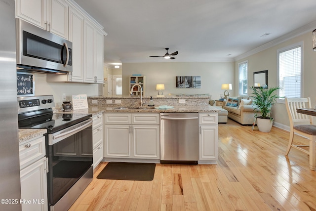 215 NE 54th St, Oak Island, NC 28465 - kitchen with stainless steel appliances, light wood finished floors, crown molding, a peninsula, and white cabinetry