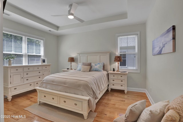 215 NE 54th St, Oak Island, NC 28465 - bedroom featuring a tray ceiling, light wood-style flooring, multiple windows, and ceiling fan