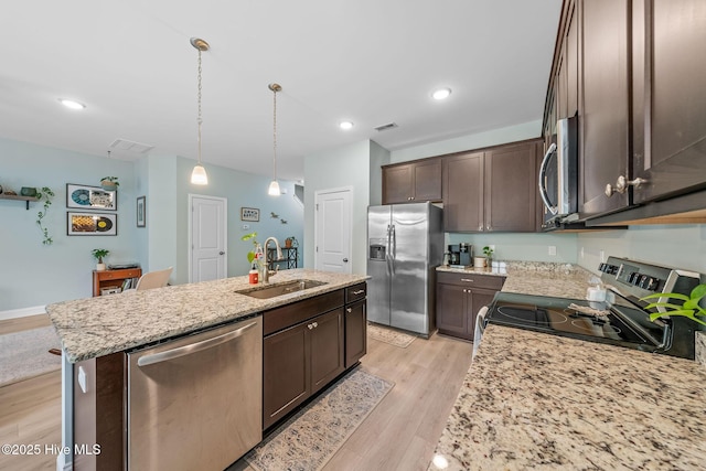 1571 Grey Cliff Run, Wilmington, NC 28405 - kitchen with appliances with stainless steel finishes, dark brown cabinetry, a kitchen island with sink, light wood-style floors, and light stone counters