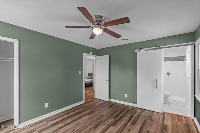 1292 Lake Cole Rd, Midway Park, NC 28544 - unfurnished bedroom featuring a barn door, wood finished floors, ensuite bath, and a ceiling fan